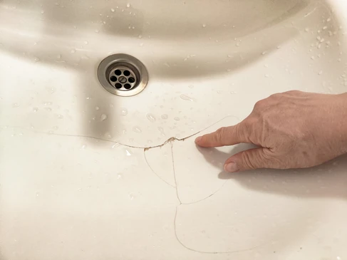 Homme en chemise bleue t&eacute;l&eacute;phonant dans salon moderne, tenant seau bleu sous fuite d'eau du plafond