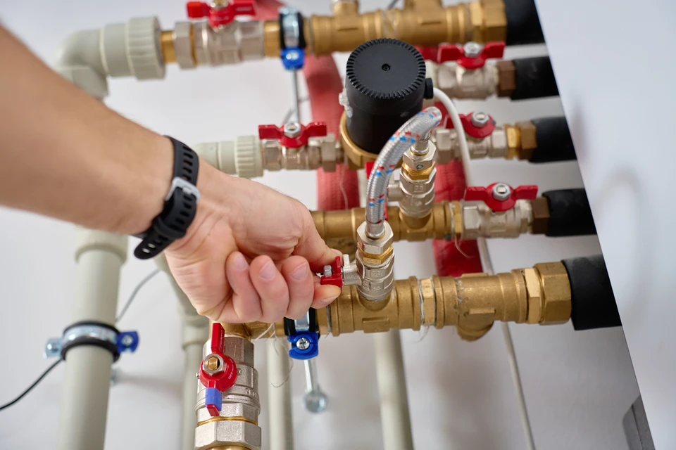 Plombier en uniforme rouge travaillant dans une chaufferie résidentielle, utilisant un outil de détection sur des canalisations en cuivre