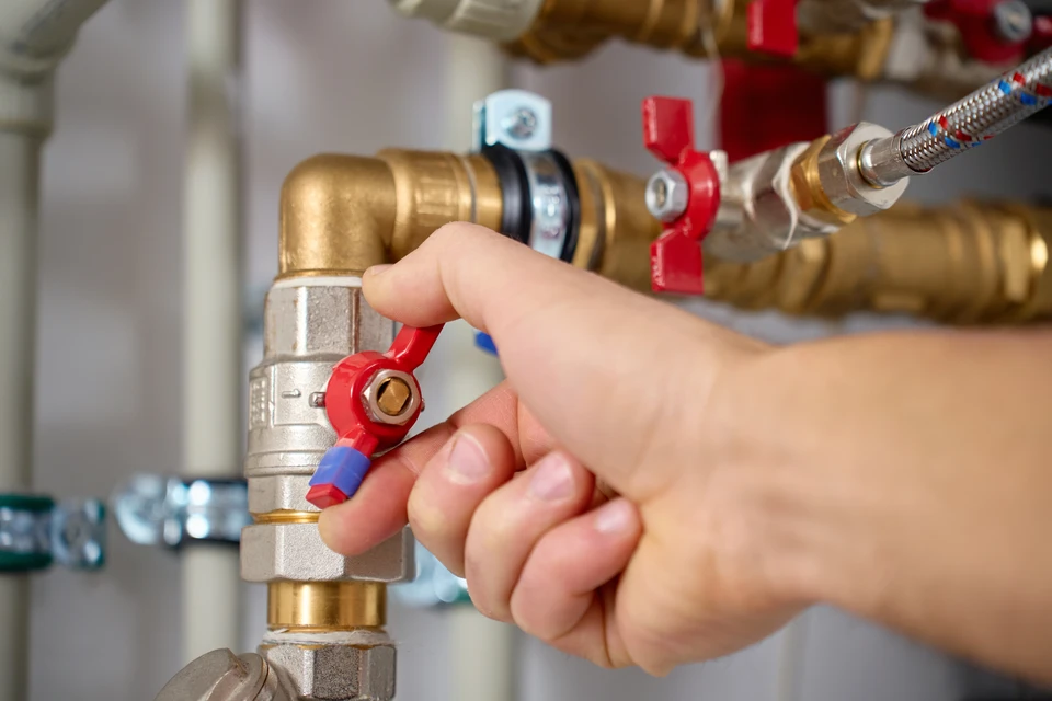 Plombier chauffagiste en tenue professionnelle travaillant sur une chaudière murale à gaz dans une cuisine résidentielle. Le professionnel est concentré sur son intervention de maintenance ou réparation, tenant ses outils. L'atmosphère doit transmettre la réactivité et le professionnalisme face à une situation d'urgence de chauffage. Photo réaliste de qualité professionnelle.